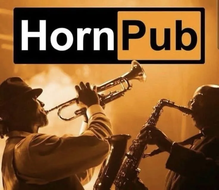 Two musicians, one playing a trumpet and the other a saxophone, are shown in a warmly lit, smoky setting. The image is…