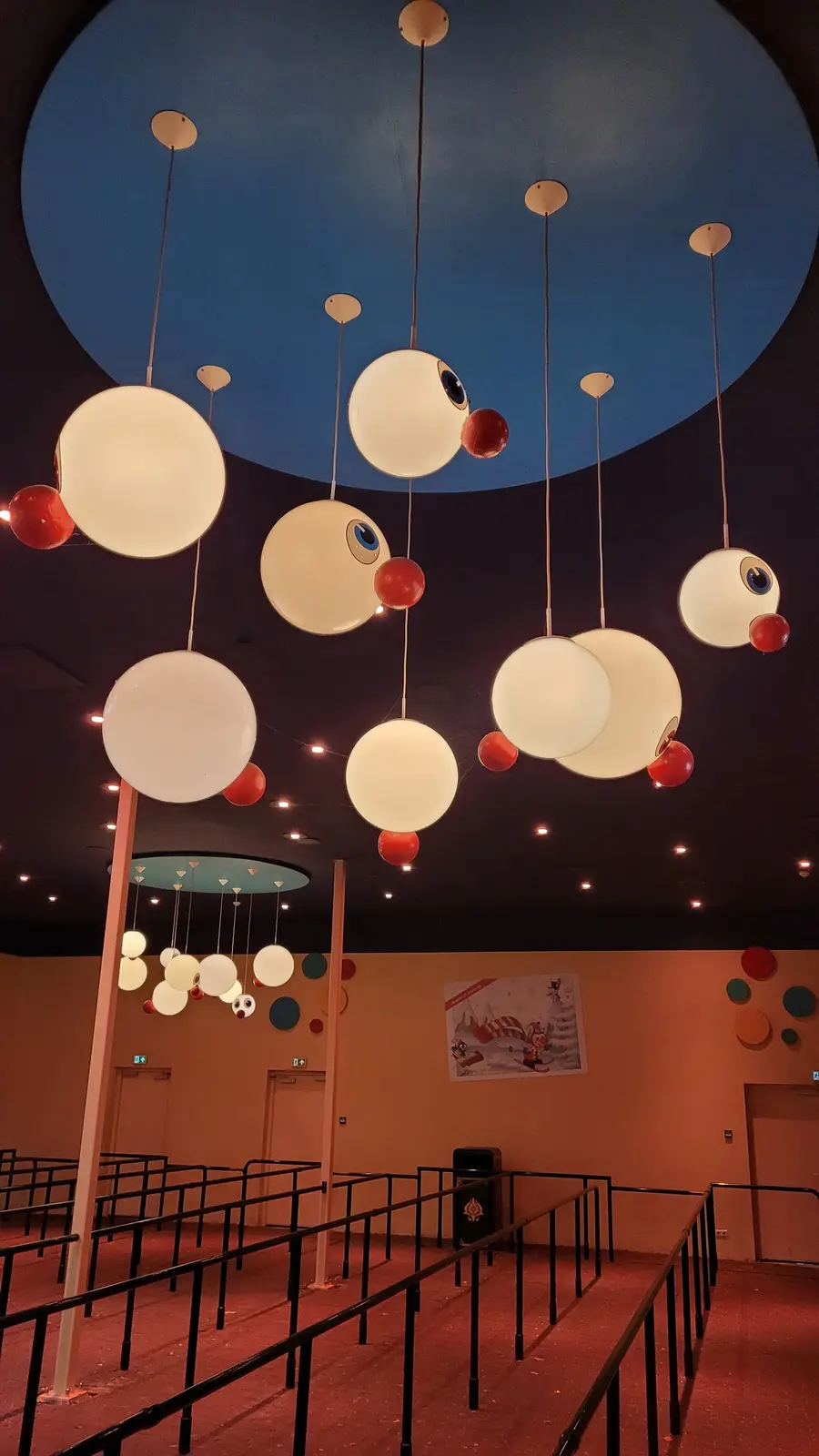 The image shows a room with a dark ceiling and a large blue circular section. Suspended from the ceiling are numerous large…