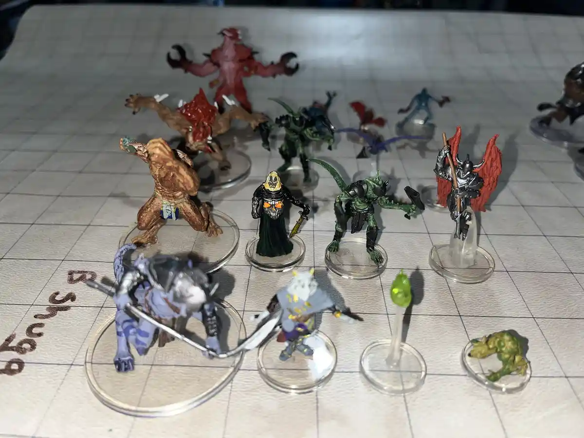 A collection of painted fantasy miniatures on a gridded battle mat, including various monsters and characters, with one…