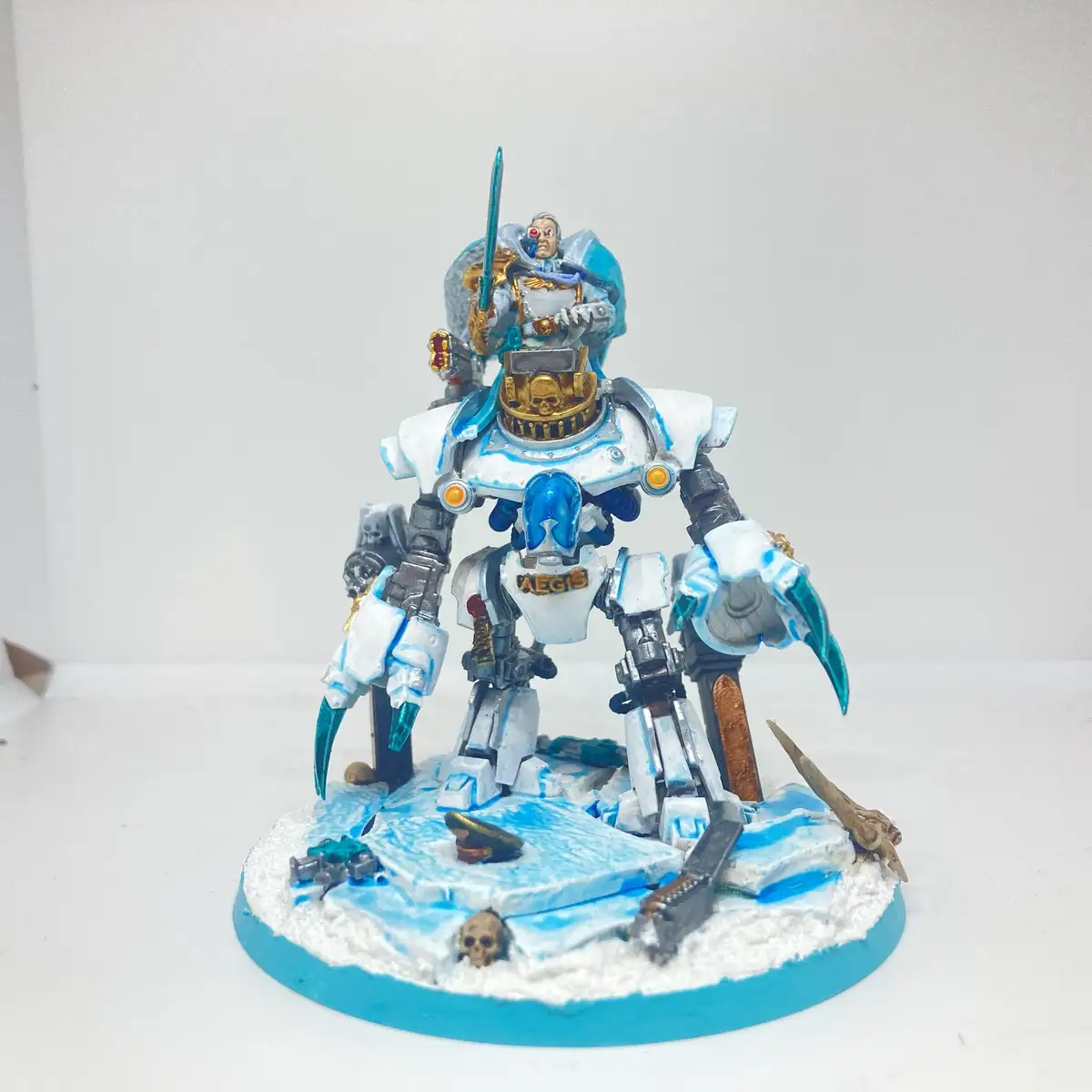 A painted miniature of a large, heavily armored robotic warrior with blue and white color scheme, standing on a circular…