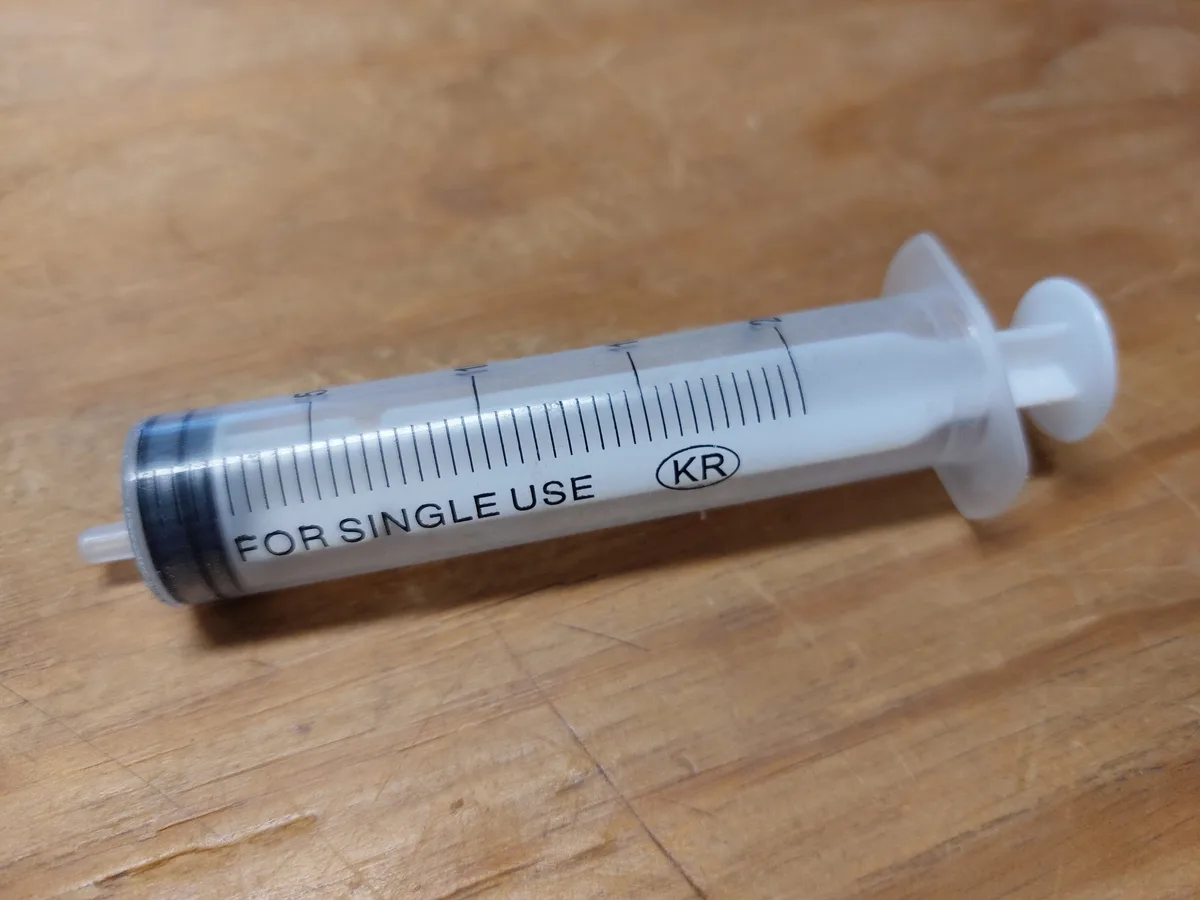 A clear plastic syringe with black measurement markings and the text 'FOR SINGLE USE' and 'KR' printed on its barrel lies…