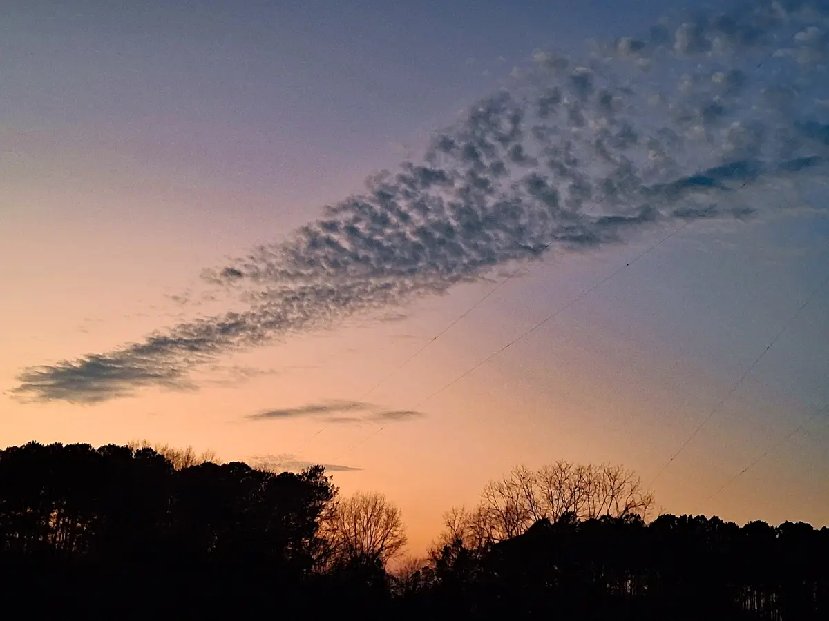 A serene sunset sky with orange and purple hues, featuring a long, textured cloud formation that resembles a giant fart…