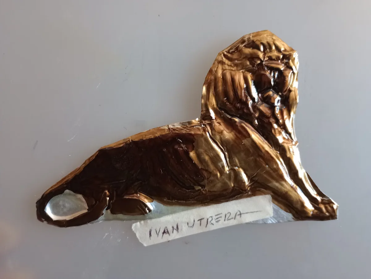 A crumpled, shiny gold-colored foil cut into the shape of a reclining lion, resting on a plain white surface with a small…