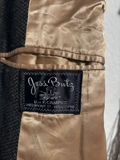 A close-up photo shows a black embroidered label sewn into the gold satin lining of a dark coat. The label reads 'Jess…