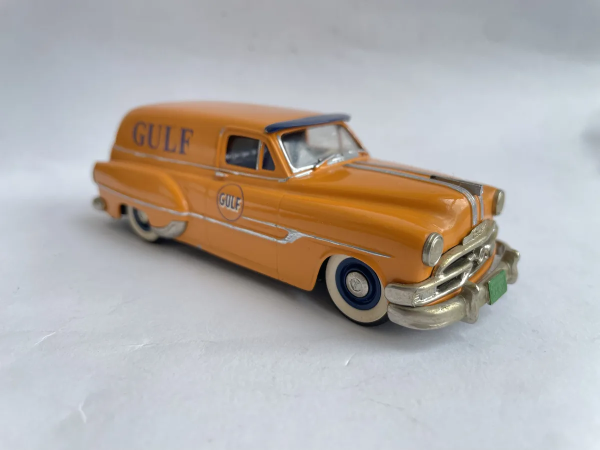A vintage orange toy delivery van with 'GULF' branding on the side and roof, featuring chrome trim, white-wall tires, and a…