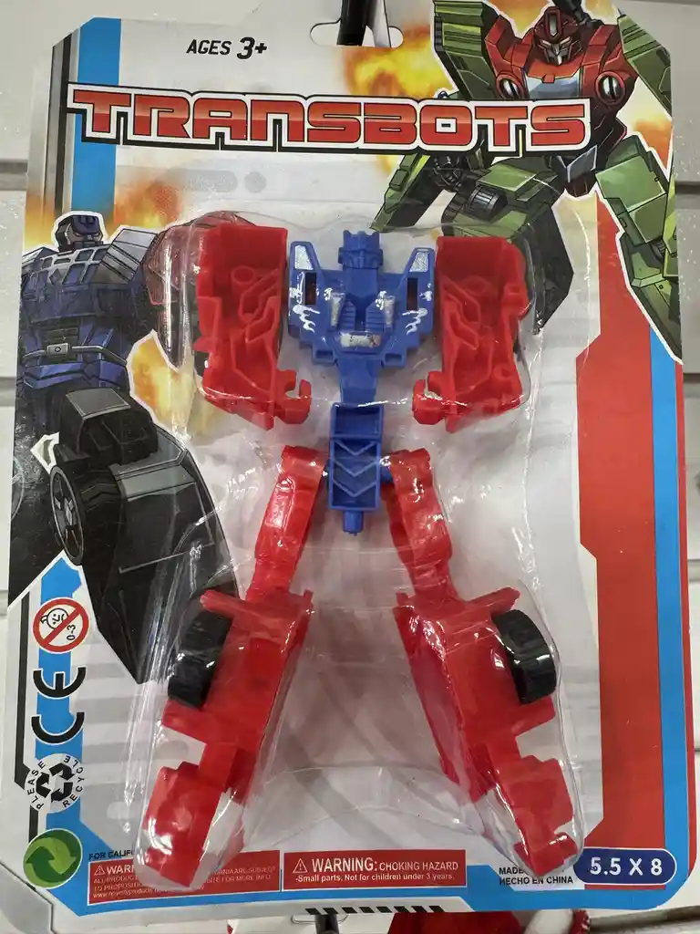 A close-up of a 'Transbots' toy package showing a small, poorly designed blue and red robot with wheels, packaged in clear…