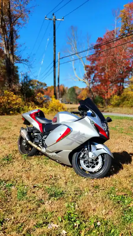 A silver and red sport motorcycle is parked on dry grass in a field during autumn, with colorful trees and power lines in…