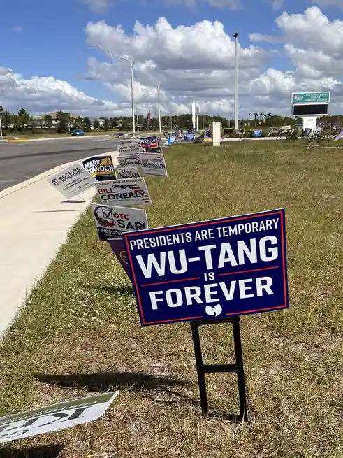 A blue political yard sign with white text reading 'PRESIDENTS ARE TEMPORARY WU-TANG IS FOREVER' and the Wu-Tang Clan logo…