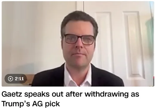 A still image from a video call shows a man with dark hair and glasses wearing a dark suit jacket over a white collared…