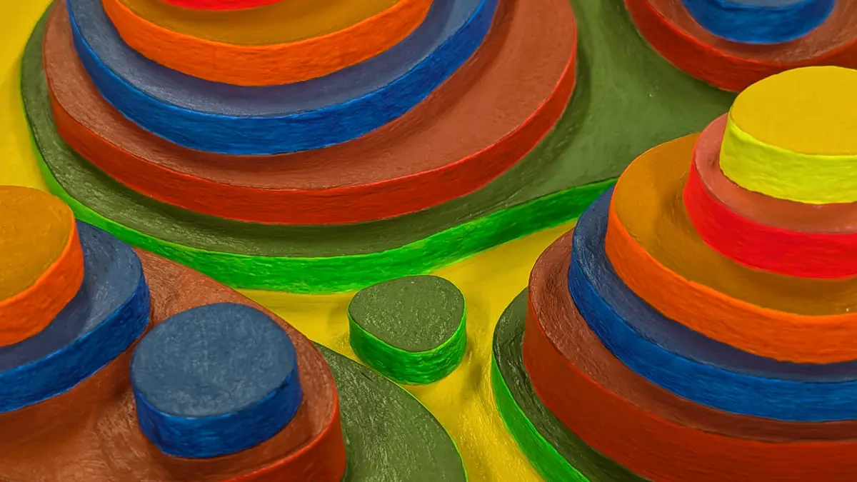 A close-up of a colorful, textured sculpture made of stacked, concentric circular discs in bright red, orange, blue, green…