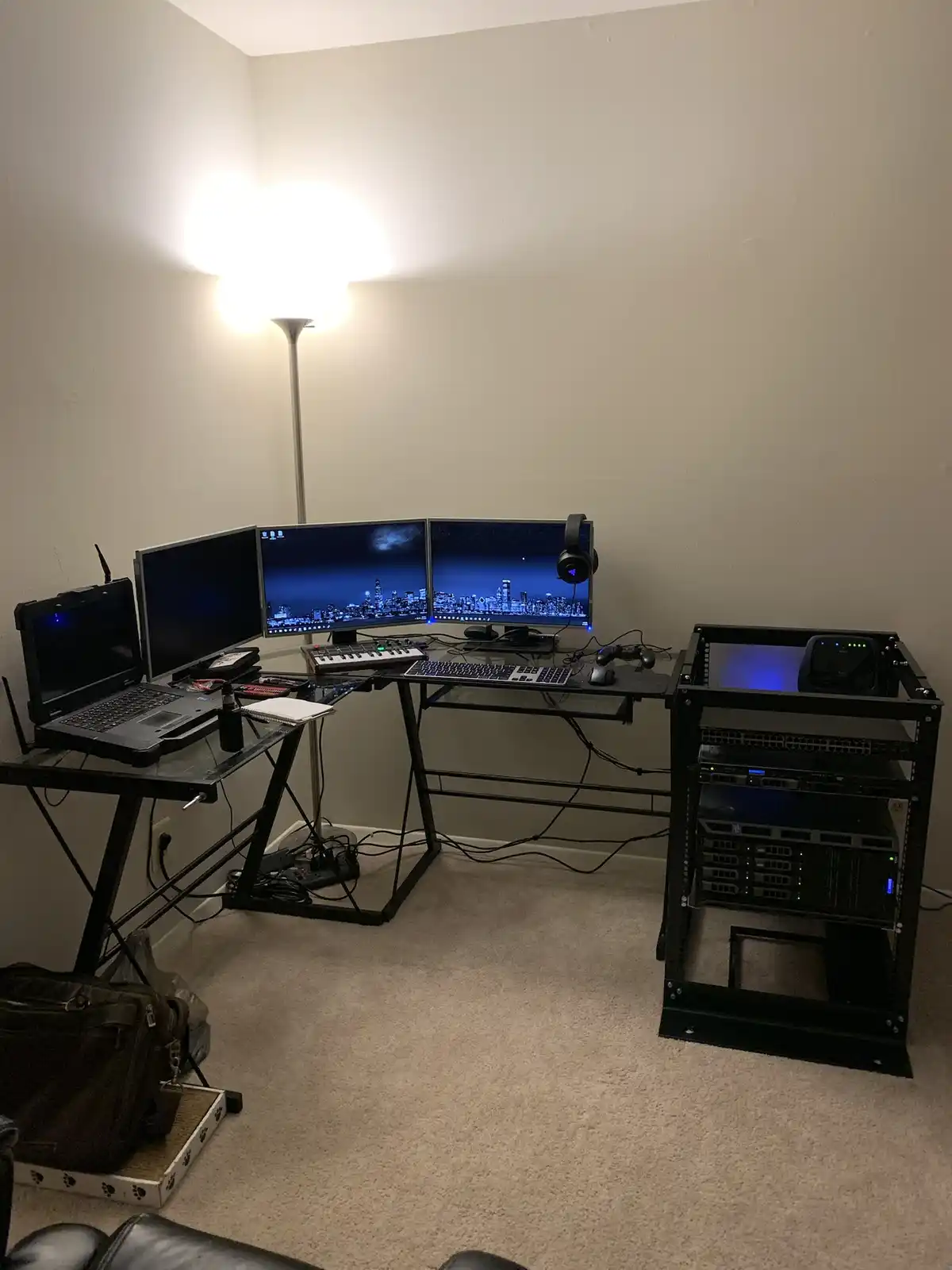 A room corner with a large, cluttered computer setup featuring multiple monitors, a keyboard, mouse, headset, and a laptop…