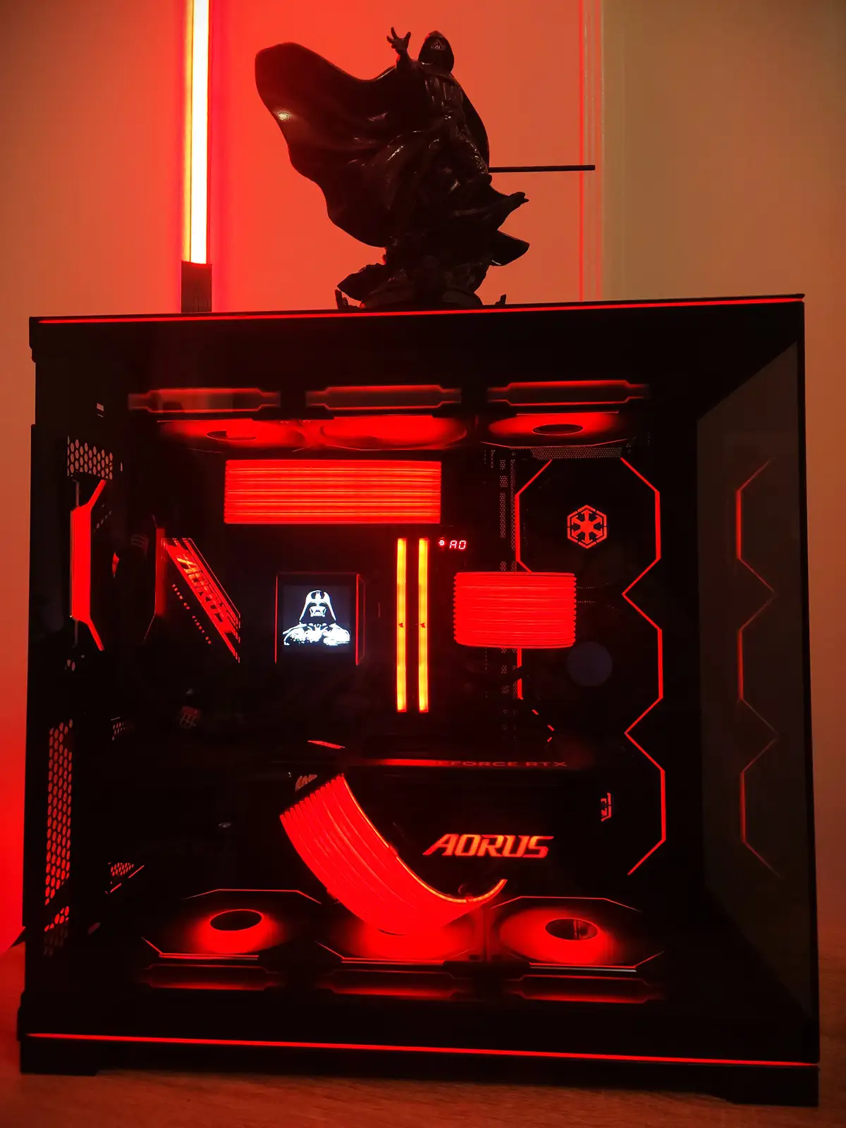 A custom-built PC case with red LED lighting is shown, featuring a Darth Vader figurine on top holding a red lightsaber…
