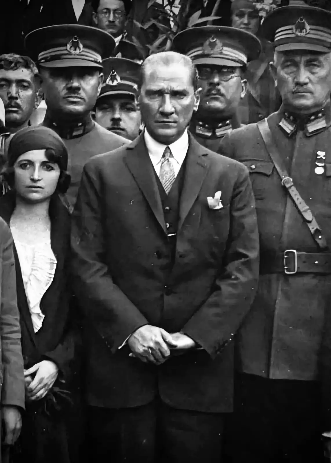 A black-and-white historical photograph shows Mustafa Kemal Atatürk standing in the center, flanked by military officers in…