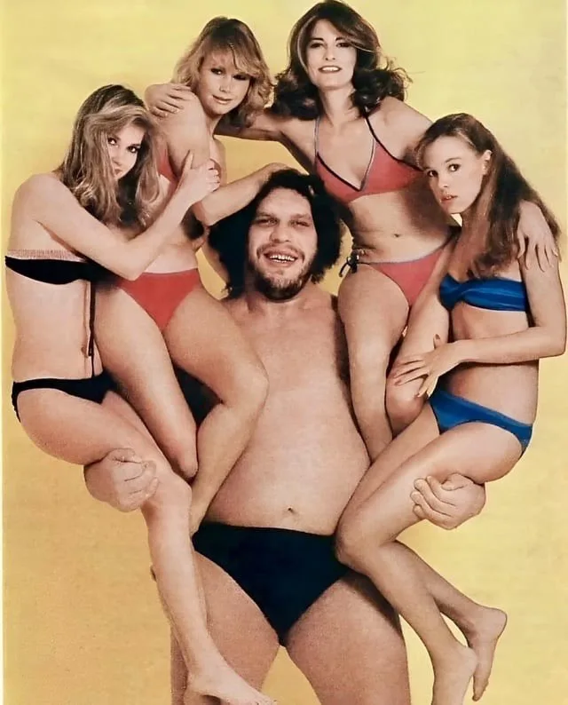 A vintage photo shows a shirtless man in black swim trunks surrounded by four women in bikinis, all posing closely around…