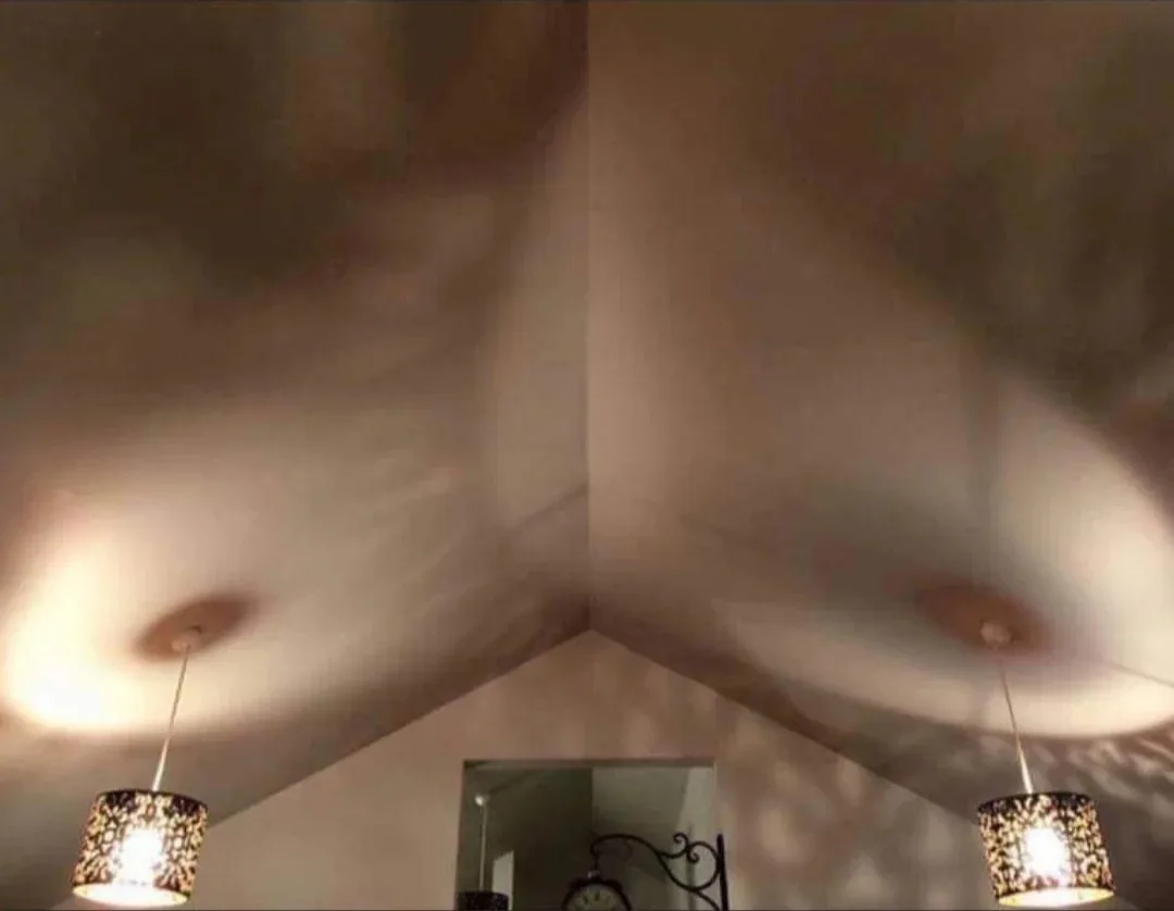 A low-angle photo looking up at a sloped ceiling with two lit pendant lamps on either side, their light casting warm glows…