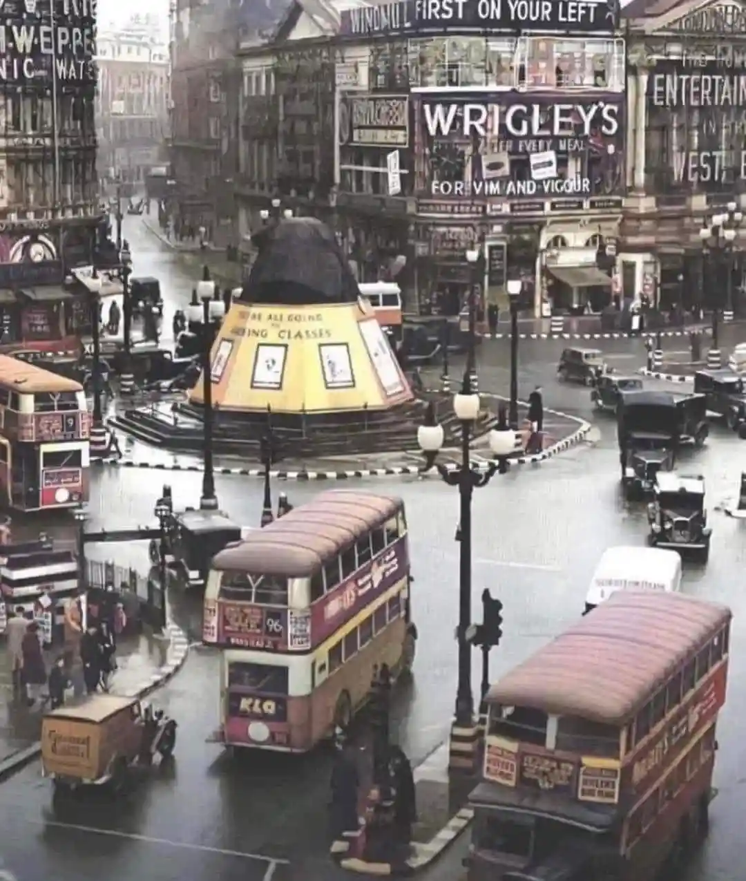 A vintage, rain-soaked street scene in London with double-decker buses and old cars, featuring a large, yellow, cone-shaped…