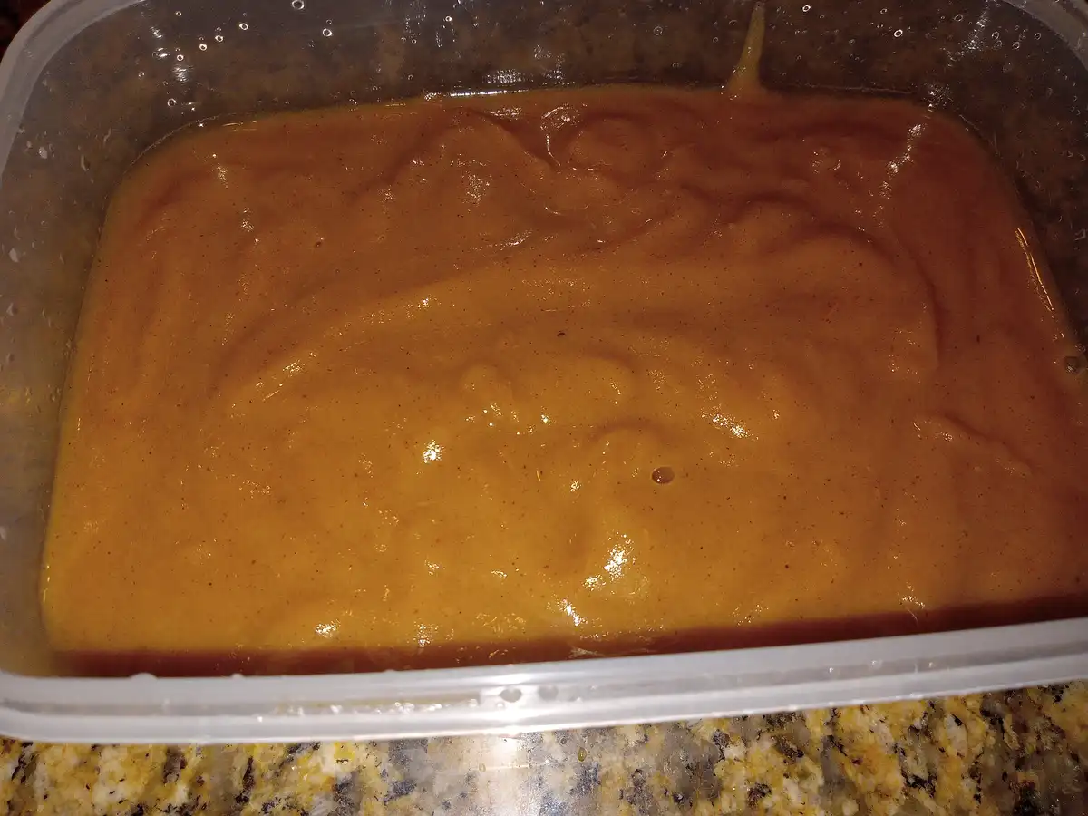 A close-up photo shows a thick, orange-brown liquid with swirls and specks in a clear plastic container, resting on a…
