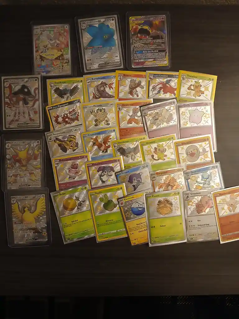 A collection of Pokémon trading cards, including various Pokémon like Alakazam GX, Pidgeot GX, and Glimmora, are arranged on…