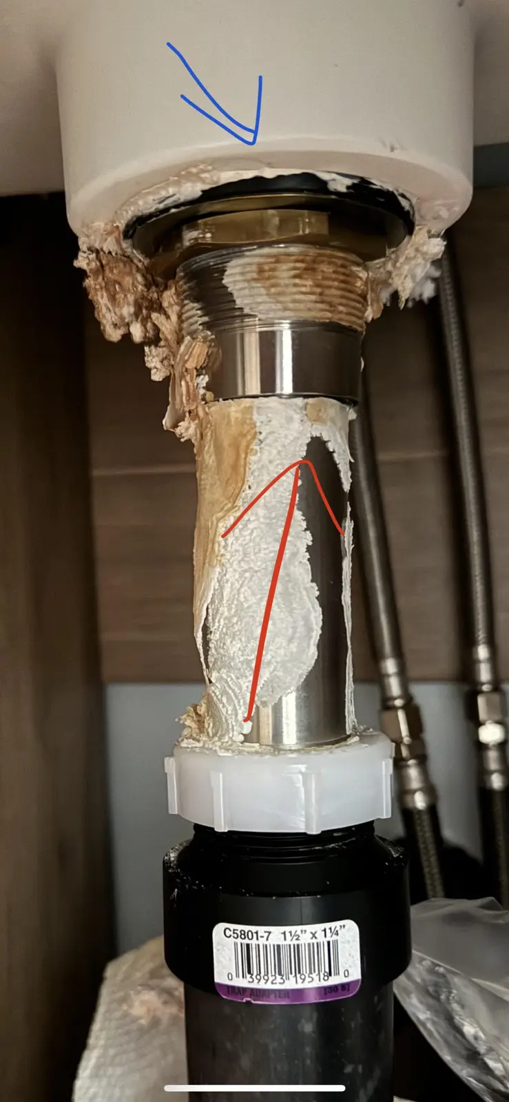 a close-up photo of a sink drain pipe showing a thick, dried, crusted white substance, likely caulk or sealant, applied…