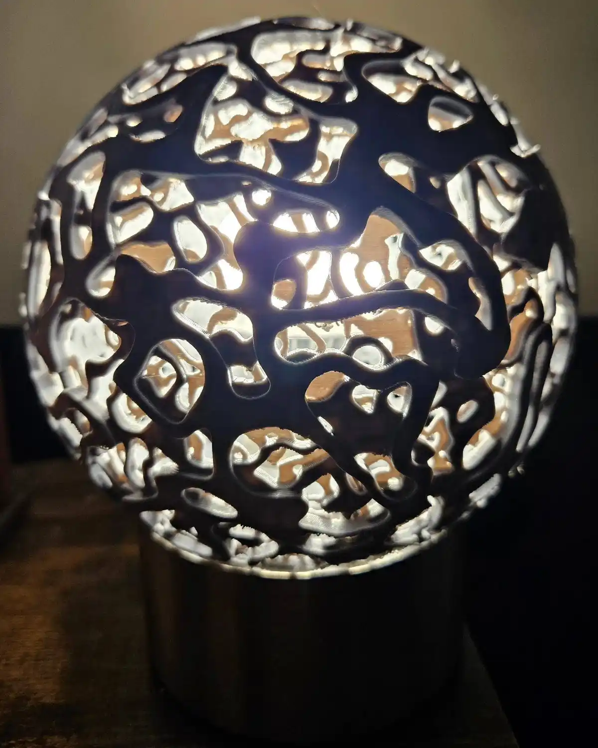 A spherical, 3D-printed lamp with an intricate, branching, organic pattern resembling a brain, glowing from within and…
