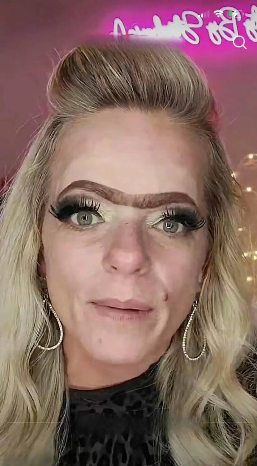 A woman with blonde hair, heavy eyelashes, and dramatic makeup looks directly at the camera with a slight smile. Her…
