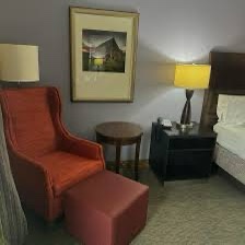 a hotel room with a red armchair and ottoman, a bed, two lamps, and a framed picture on the wall. overlaid text reads 'this…