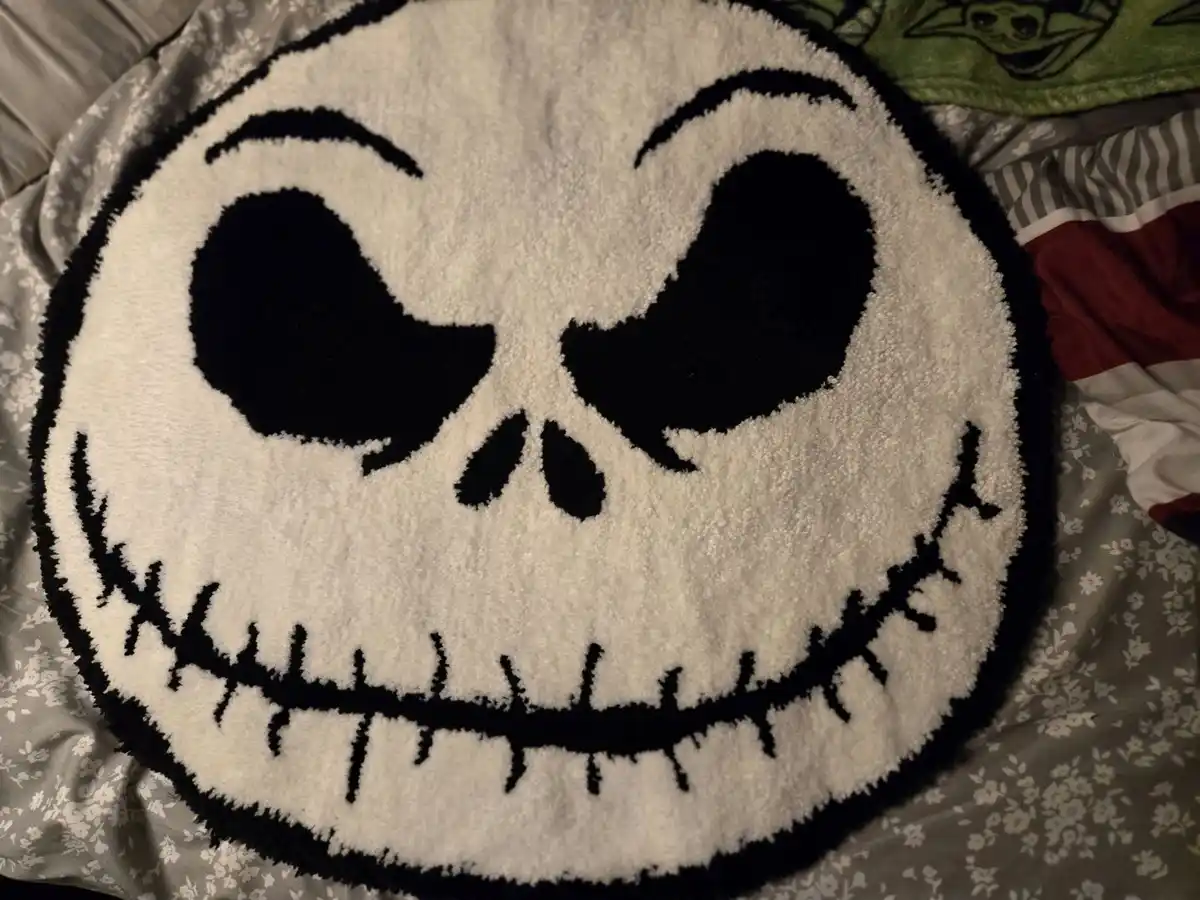 A circular, fluffy rug featuring the iconic stitched smile and large eyes of Jack Skellington from The Nightmare Before…