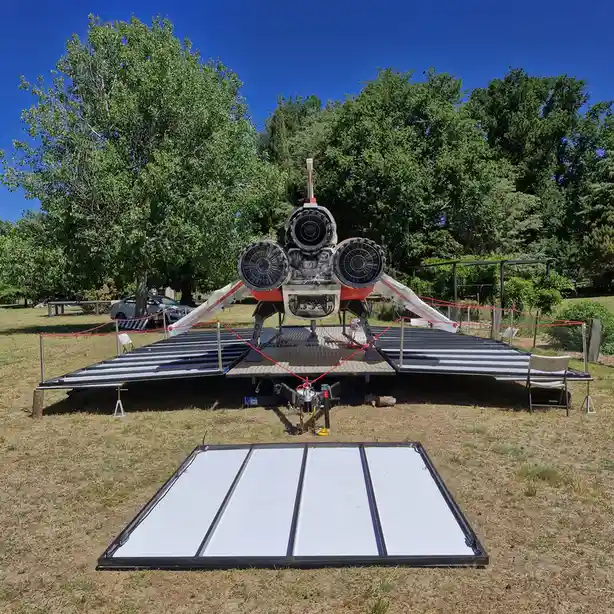An outdoor display features the rear of a jet engine with three visible turbine fans mounted on a metal platform, surrounded…