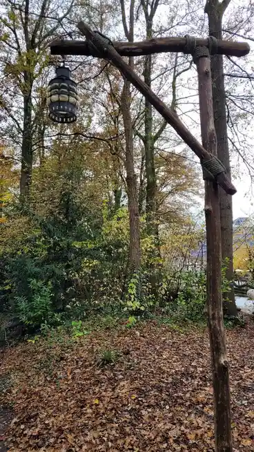 A rustic wooden frame made of rough-hewn branches and thick rope is set up in a leaf-strewn autumn forest, with a modern…