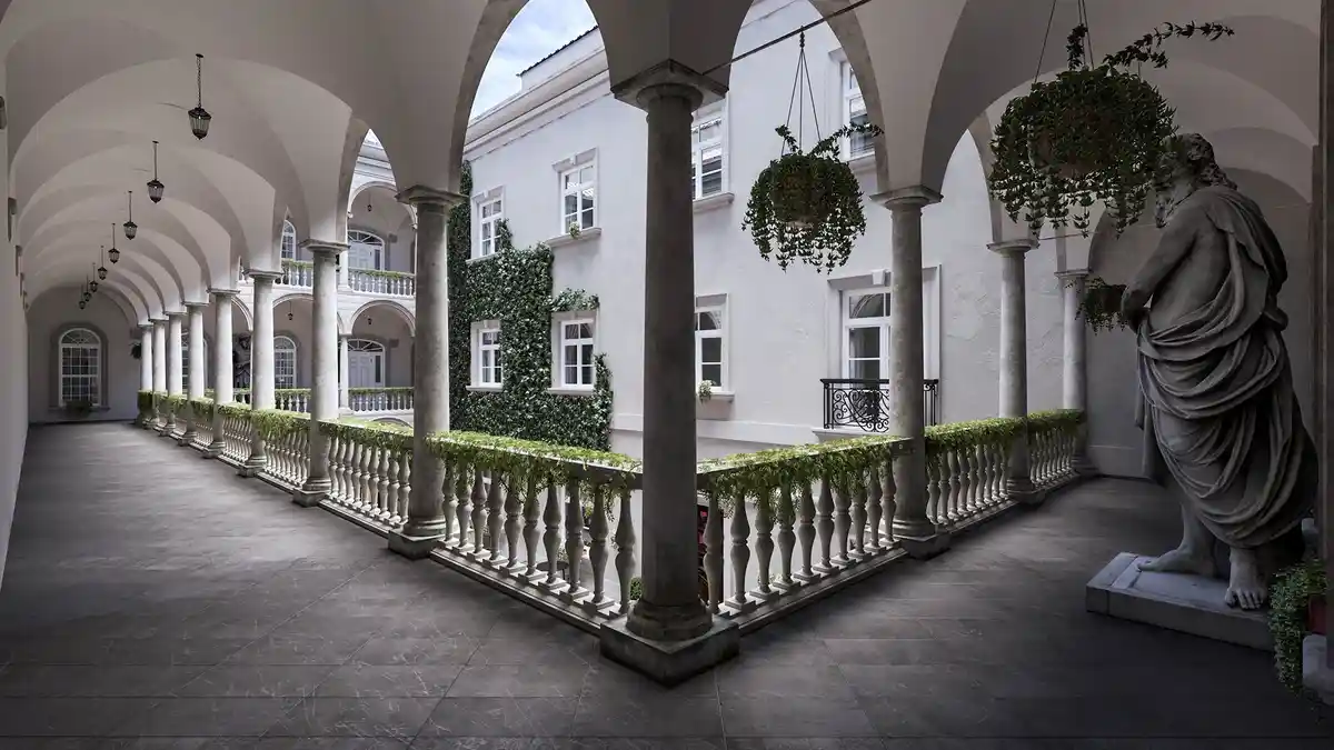 A grand, classical courtyard with stone arches, columns, and a statue of a robed figure, overlaid with the text 'i'm not a…