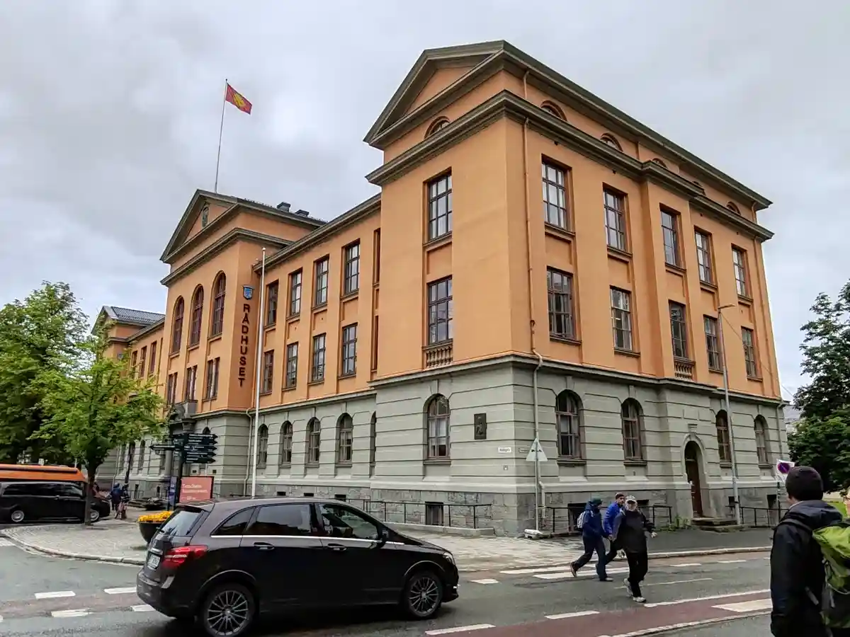 A photograph of a large, peach-colored municipal building with gray stone foundations and arched windows, identified by…