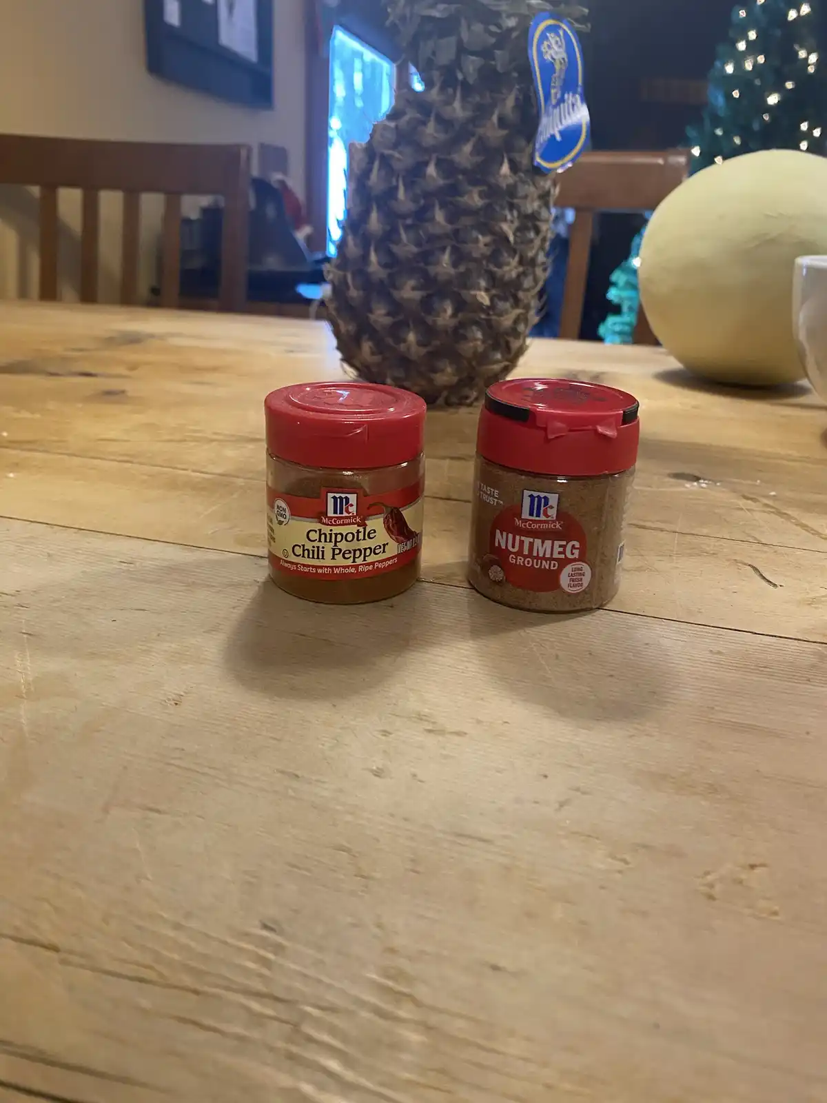 Two small McCormick spice jars sit side-by-side on a wooden table; one is labeled 'Chipotle Chili Pepper' and the other…