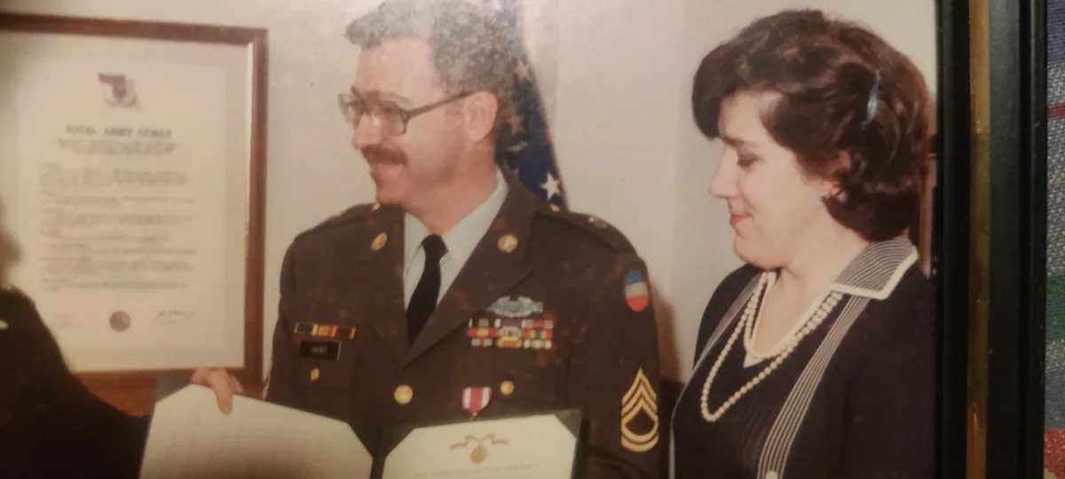 A vintage photo shows a smiling man in a decorated U.S. Army uniform standing beside a woman in a dark dress with pearls…