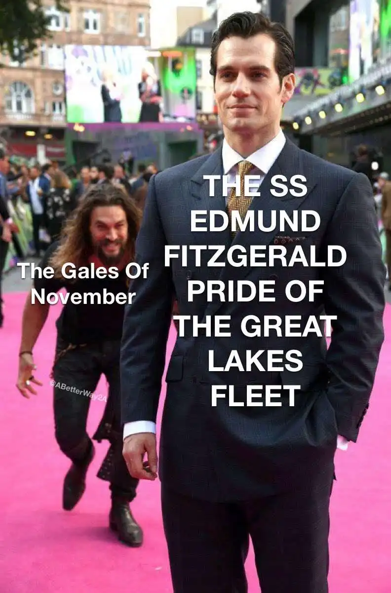 A man in a suit stands confidently on a pink carpet with text overlaid on his chest reading 'THE SS EDMUND FITZGERALD PRIDE…