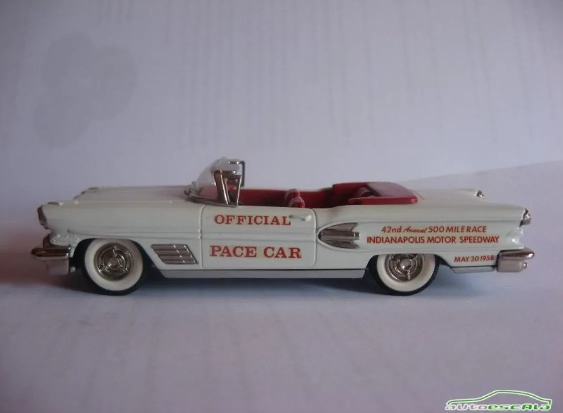 A white die-cast model of a 1958 Cadillac convertible pace car, featuring red interior and chrome details, with red text on…