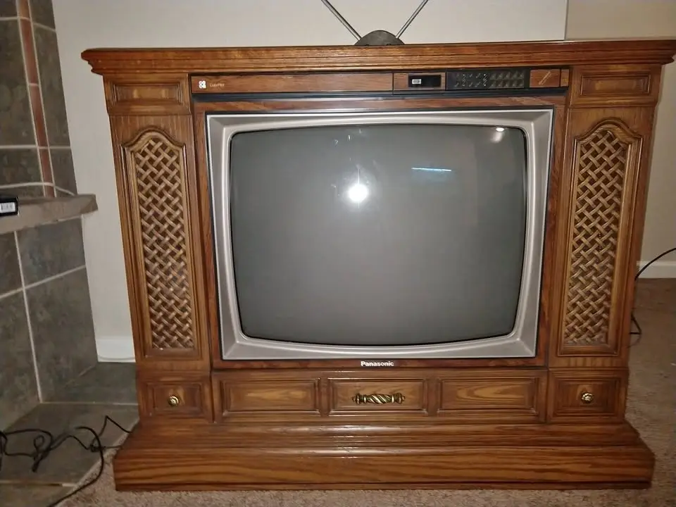 A vintage Panasonic CRT television set, housed in an ornate wooden entertainment center with lattice-patterned side panels…