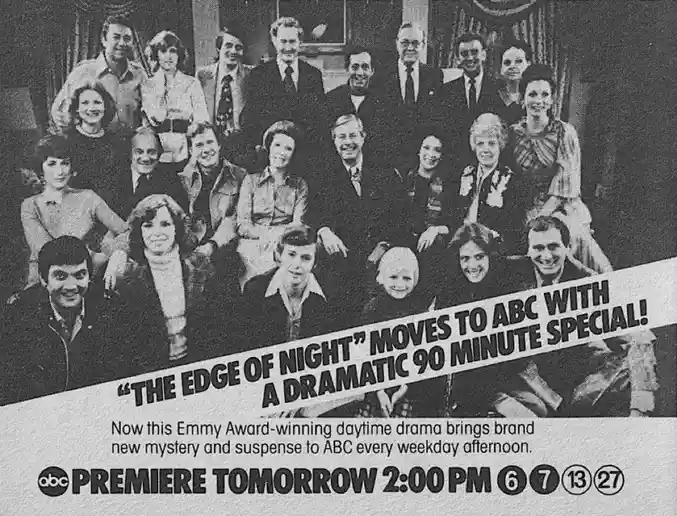 A black-and-white vintage TV advertisement photo shows a large group of actors posing formally in a studio setting. The…