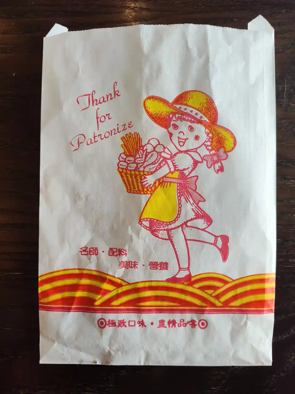 A crumpled white paper bag from a fast-food restaurant features a cartoon girl in a yellow hat and dress carrying a basket…