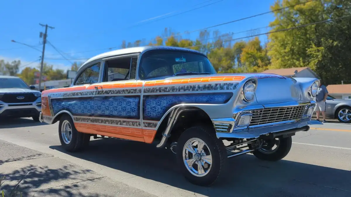 A custom hot rod with a blue and orange paint job and chrome details is parked on a street under a clear blue sky. The car…