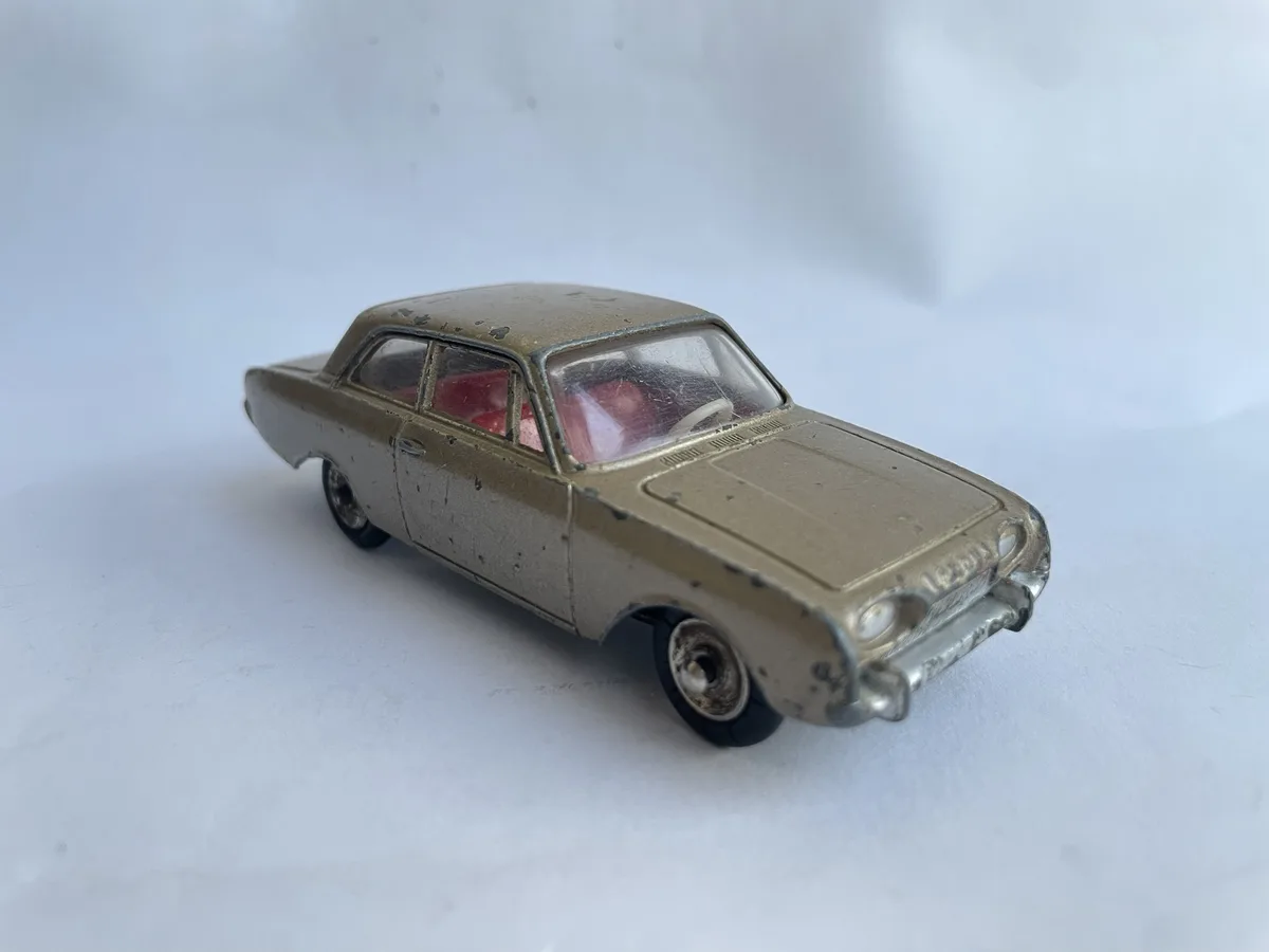 A weathered, gold-colored vintage toy car with chipped paint and visible wear sits on a plain white surface. The car's…