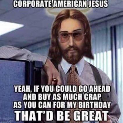 A man with long hair, a beard, and sunglasses, dressed in a business suit and tie, stands in an office cubicle environment…
