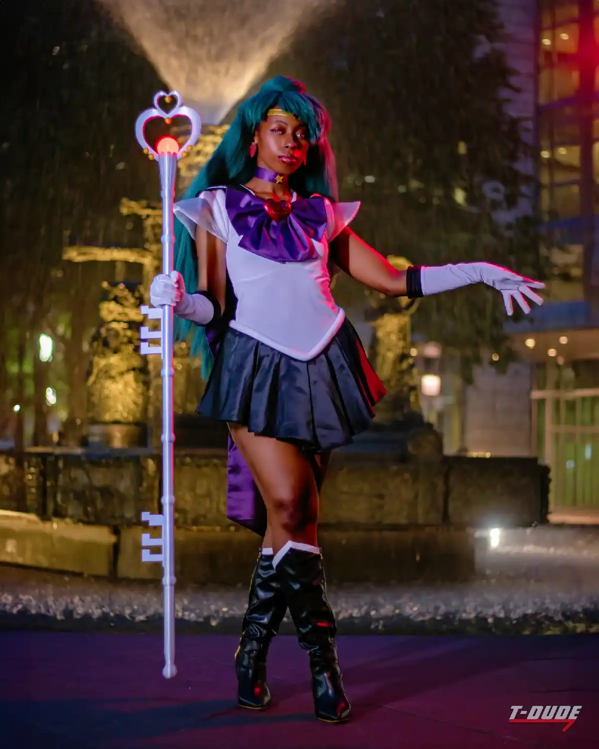A person in a Sailor Moon cosplay, holding a glowing key-shaped staff, poses confidently in front of a fountain at night…