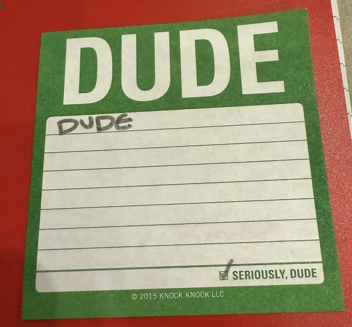 A green 'DUDE' notepad with 'DUDE' handwritten in the first line and 'SERIOUSLY, DUDE' checked off at the bottom, set…
