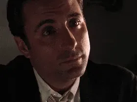 six sequential frames show a man in a dark suit and tie, transitioning from a serious, intense gaze to closing his eyes and…