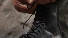 Six stills from the movie 'Predator' show Arnold Schwarzenegger preparing for battle: lacing combat boots, wearing a vest…