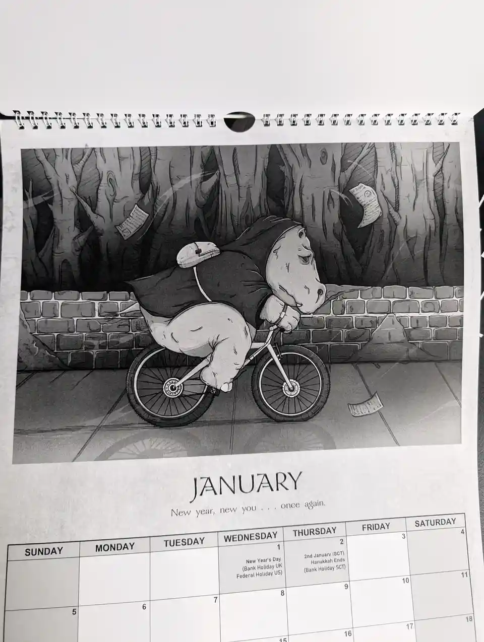 A black-and-white calendar page for January shows a cartoon hippo in a hooded cloak riding a bicycle with a weary…