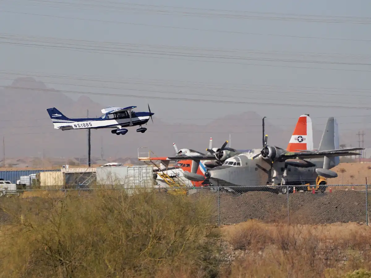A small blue and white single-engine airplane with registration N51885 is flying low over a desert area, passing above…