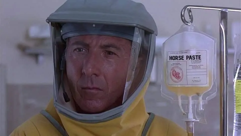 A man in a yellow hazmat suit with a clear face shield looks concerned while standing next to an IV bag labeled 'HORSE…