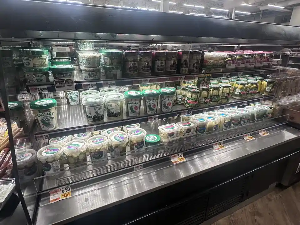 A refrigerated grocery store aisle filled with various brands of pickles, including Grillo's and Claussen, with price tags…