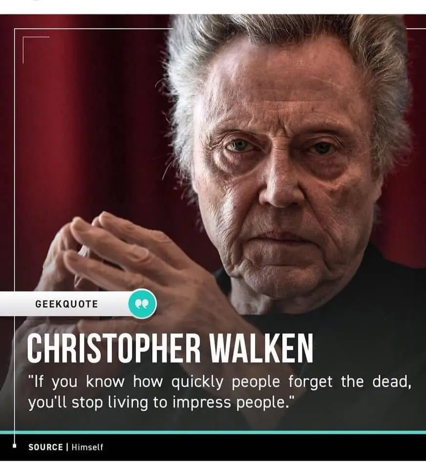 A close-up photo of actor Christopher Walken with a serious expression, hands clasped, against a red curtain background…